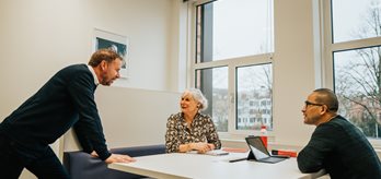 Drie medewerkers in gesprek aan een tafel